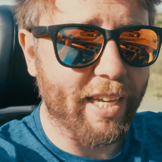 Dom Smith in sunglasses, filming himself from the driver’s seat of a convertible.
