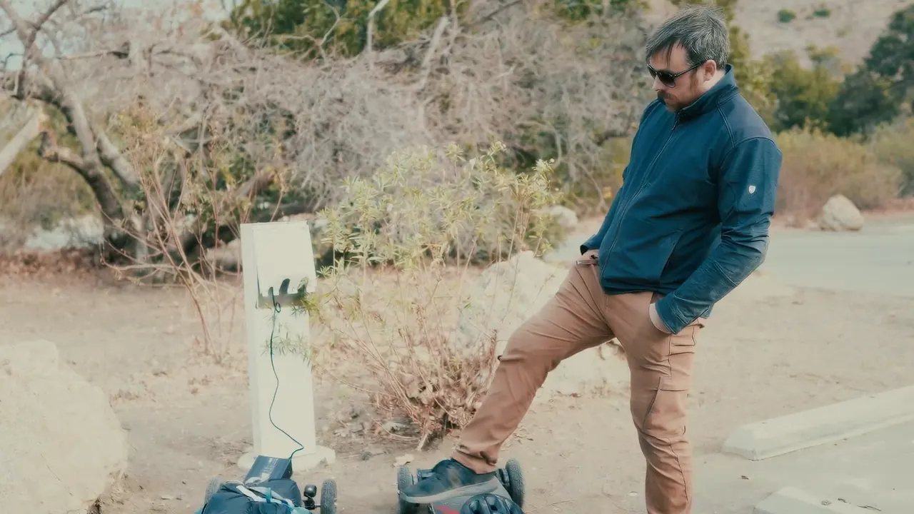 A rider standing by his board, plugged into a power post at a campground.