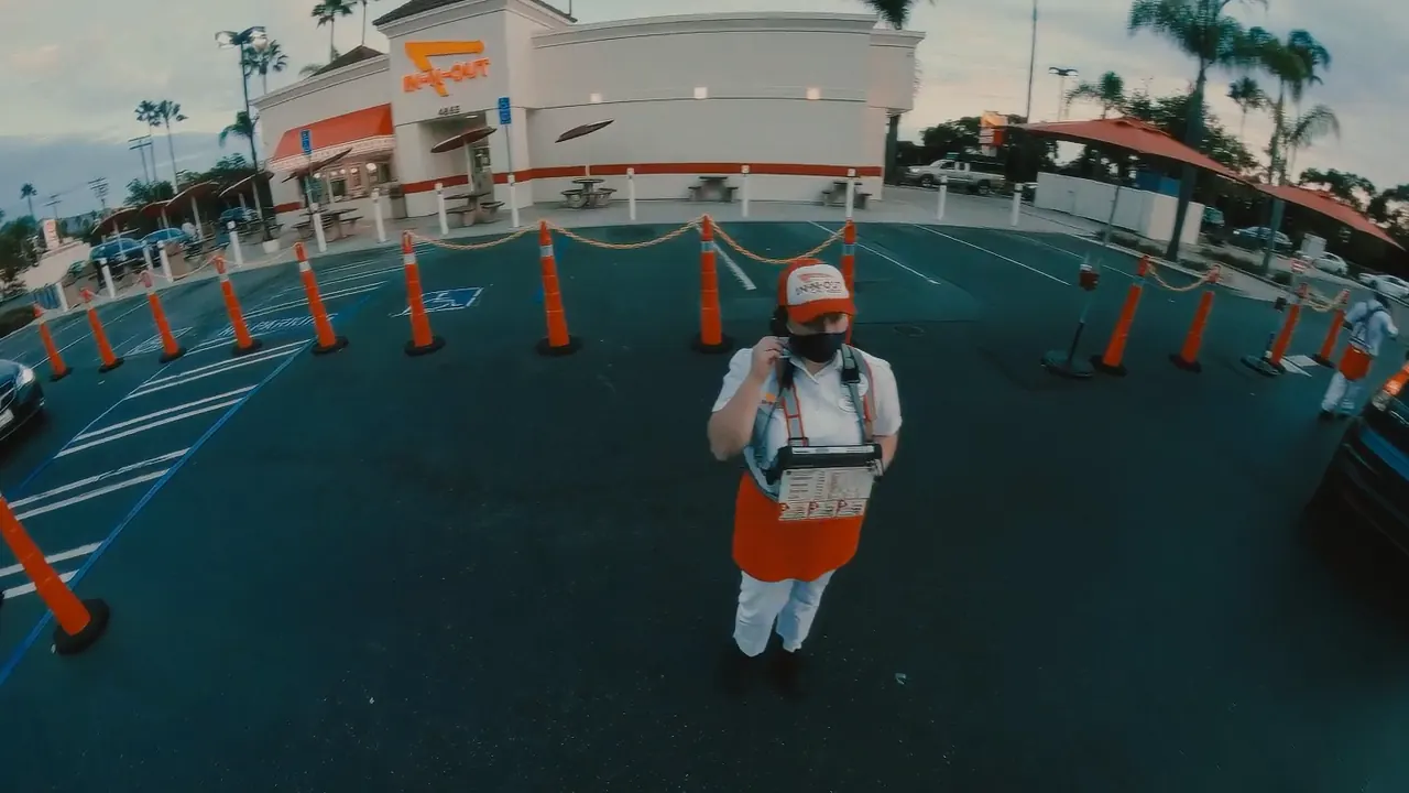 A rider in a helmet among the traffic cones of an In-N-Out car park.