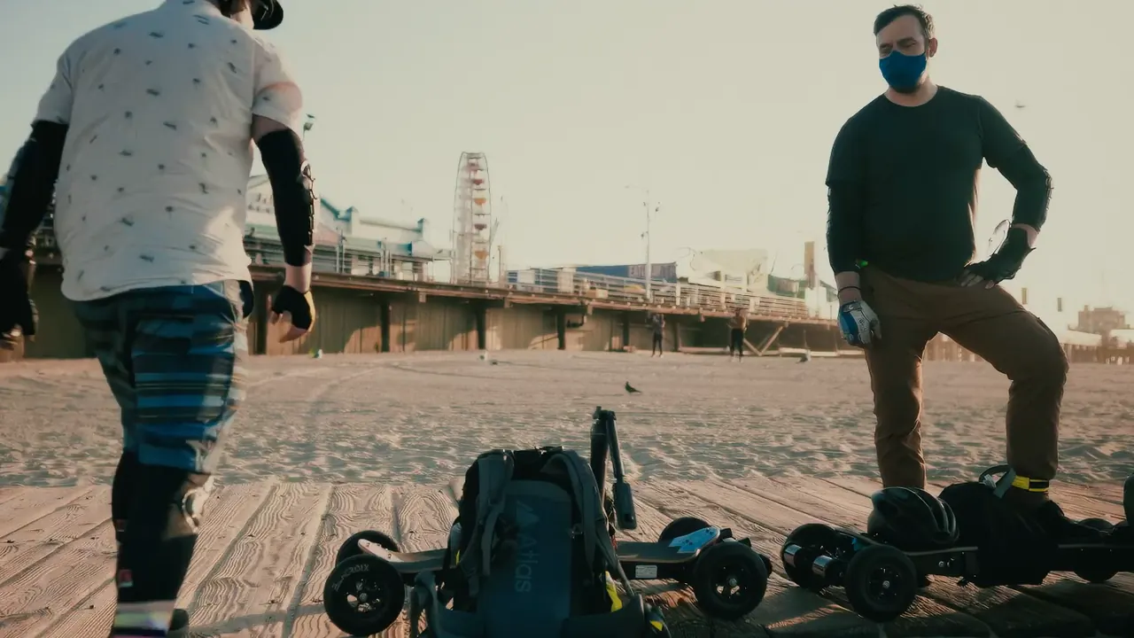 The two riders on the sand at Santa Monica with their boards, the pier behind them.